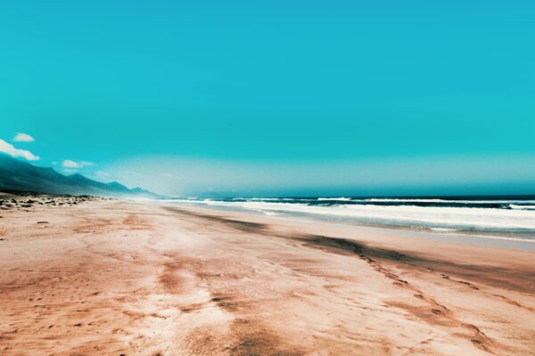 A pristine sandy beach with turquoise skies and gentle waves, perfect for travel enthusiasts.